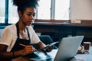 Kahve dükkanında kendine güvenen zenci bir kadının portresi. İş için dizüstü bilgisayarda çalışırken gülümsüyor. Finans muhasebesini azimle yöneten serbest meslek sahibi girişimci.