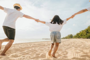 Mutlu Asyalı ebeveynler ve kızları sahilde eğleniyorlar. Kumda koşan ve rol yapan anne ve babalarıyla küçük kızlar. Olumlu aile aktivitesi