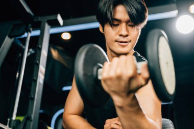 Asyalı kaslı adam ağırlık kaldırıyor, spor salonunda ağırlık çalışırken dambıl kullanıyor spor salonunda kaslarını şişiriyor, sağlıklı yaşam tarzı kavramını geliştiriyor.