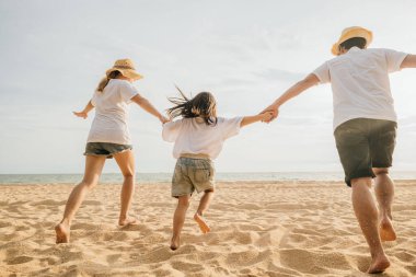 Mutlu Asyalı ebeveynler ve kızları sahilde eğleniyorlar. Kumda koşan ve rol yapan anne ve babalarıyla küçük kızlar. Olumlu aile aktivitesi