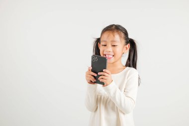 Beyaz arka planda izole edilmiş akıllı cep telefonu stüdyosunu kullanarak heyecanla gülümseyen mutlu Asyalı genç kız portresi.