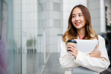 Gülümseyen genç bir kadın elinde bir fincan sıcak kahve ve gümüş bir dizüstü bilgisayarla duvara doğru yürüyor. Güzel yaz günü, ara verirken verimlilik ve rahatlama ile doludur..