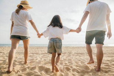 Mutlu Asyalı ebeveynler ve kızları sahilde eğleniyorlar. Anne ve babalarıyla birlikte kumsalda yürüyen bir çocuğun elini tutan küçük kızlar. Olumlu aile aktivitesi