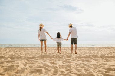 Mutlu Asyalı ebeveynler ve kızları sahilde eğleniyorlar. Anne ve babalarıyla birlikte kumsalda yürüyen bir çocuğun elini tutan küçük kızlar. Olumlu aile aktivitesi