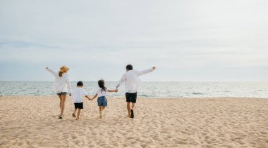 Ebeveynler ve çocuklar sahilde el ele tutuşarak ve bayram eğlencesinde zıplayarak neşeli anılar yaratıyorlar. Sahil tatilinin kaygısız ruhunu gösteren bir aile seyahati konsepti..