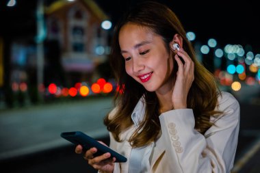 Genç bir kadın, bir telefon görüşmesi için kulaklığını şehir caddesinde kullanıyor. Geniş bant servisi kusursuz iletişim sağlıyor. El bilgisayarı teknolojisi.