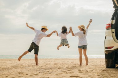 Mutlu aile üç el ele verip kumsalda zıplar, anne ve babalar çocuklarının arabasına atlayıp, yaz tatiline çıkarlar, yaz gezisine çıkarlar, aile günlerini birlikte geçirirler.