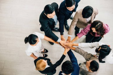 Dört farklı iş adamı, sembolik bir yığın oluşturan üst bir bakış açısından bir daire şeklinde el ele tutuşuyorlar. Bu resim birlik takım çalışmasını ve küresel işbirliğini temsil ediyor.