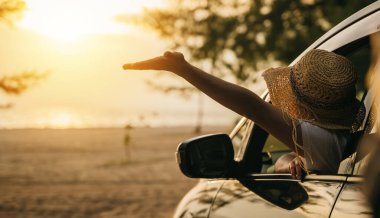 Hasır şapkalı bir kadın gün batımında el sallayarak arabanın ön koltuğunda oturur ve rüzgarı hisseder. İyi hafta sonları. Plajda iyi tatiller. Yaz tatili yolculuk konsepti