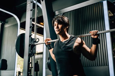 Asyalı kaslı adam spor yapıyor. Ağırlık çalışıyor. Spor salonunda halterle ağırlık çalışıyor. Erkek halter kaldırıyor.