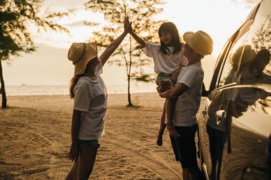 Asyalı aile gün batımında araba vitrininde oynarken tatillerde ve dinlenirken tuhaf hissediyorlar. İyi hafta sonları. Plajda iyi tatiller. Yaz tatili yolculuk konsepti