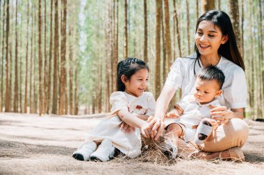 Asyalı aile fertleri yemyeşil orman doğasını kucaklıyor, mutlu anne kız ve erkek çocukla piknikte oturuyor, aile tatili.