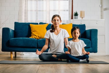 Bir anne ve kızı, aile yogasında huzur bulurlar. Nilüfer pozisyonunda oturup farkındalık ve meditasyona odaklanırlar. Evde mutluluğu ve birlikteliği teşvik ederler..