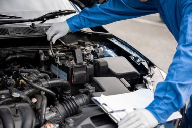 Üniformalı Asyalı tamirci gülümsüyor. Garajda pano ile arabanın motorunu kontrol ediyor. Araba servisi ve teknolojik tamirat konusunda uzmanım. Otomotiv endüstrisinde iş. Kontrollü adam bakım yapıyor..