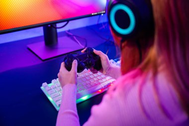 Gamer using joystick controller for virtual tournament plays online video game with computer neon lights, woman wear gaming headphones playing live stream esports games console at home