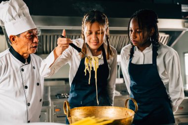 Mutfakta aşçı öğretmenleri. Öğrenci kızlar Japon eriştesi hazırlar. Çocuklar ve öğretmen ocakta. Öğrenmenin gülümseyen portresi modern eğitimdir. Kepçeyle yemek yapmak neşe veriyor..