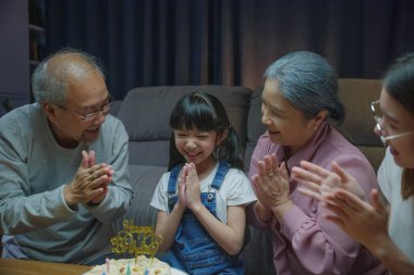 Mutlu Asyalı aile büyükbabaları ve anneleri doğum günü partisinin tadını çıkarıyor. Torunlarının pastasıyla evde mum üflüyorlar. Doğum günü sürprizi konsepti.