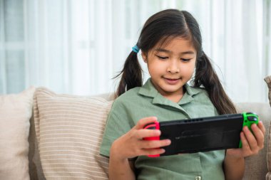 Kanepede otururken tablet kullanan mutlu Asyalı genç kız evdeki oturma odasında video oyunu oynayan çocuk, online oyun konsepti.