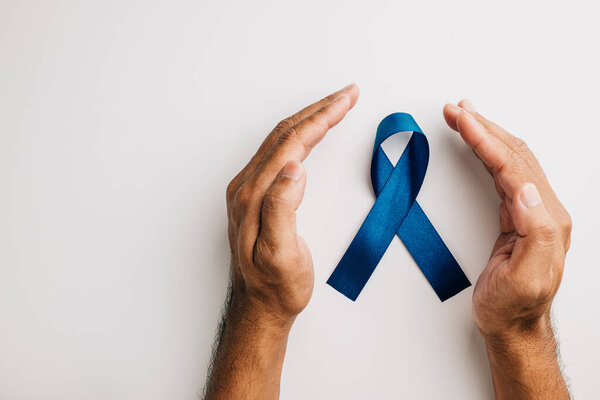 Мощный символ заботы о здоровье в ноябре, руки держат синюю ленту на белом заднем фоне. Поддержка больных раком простаты и их семей.