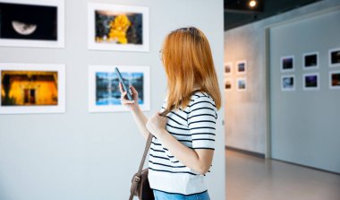 Ziyaretçi kadın önünde resim galerisi koleksiyonu cep telefonlu resimler, sanat galerisindeki akıllı telefonlu fotoğraf çerçevesini izleyen Asyalı kadın.