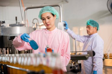 QC rolündeki mühendisler fabrikadaki cam şişelerde meyve suyu üretimini denetliyor. Onların dikkatli incelemeleri imalatta en yüksek kaliteyi ve temizliği sağlar..