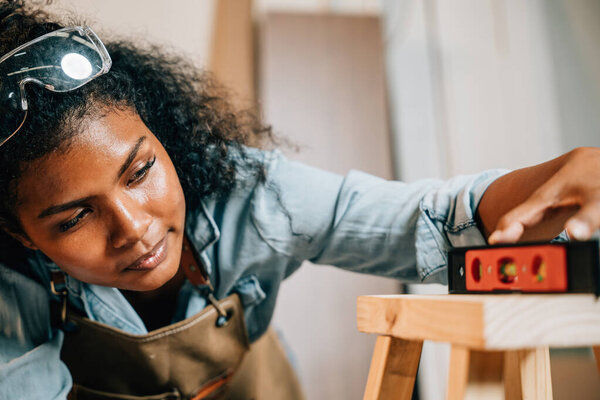 Афроамериканская плотница использует уровень на деревянном стуле в мастерской. Мастер столярных мастерски изготовление массивной сосновой мебели, окруженный инструментами и материалами, Национальный день плотников