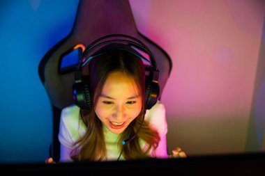 Asyalı mutlu oyuncu oyunu bilgisayar neon ışığı ile çevrimiçi video oyunları turnuvası düzenliyor, oyun kulaklığı takan gülümseyen genç kadın evde canlı yayın oyunları oynamak niyetinde, yazı tipi görünümlü