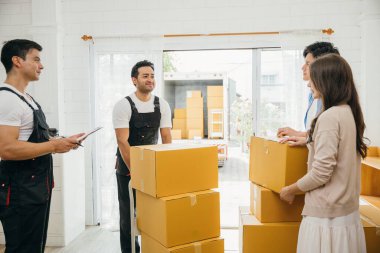 Taşınan belgeleri imzalamadan önce aile listedeki kutuları inceler. İşçi bir kutu tutuyor. Profesyonel nakliyeciler kesin yer değiştirme servisi sağlar. Takım çalışması ve ev taşınması apaçık ortada. Taşıma Günü
