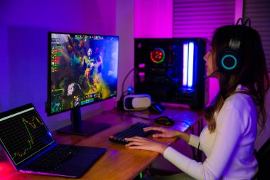 Masaüstü bilgisayar ekranında çevrimiçi video oyunu oynayan Asyalı profesyonel oyuncu renkli neon ışıklı ışıklara, evde oyun oynamak için bilgisayar kullanan oyun kulaklıklarına sahiptir