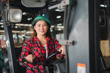 Fabrikada Asyalı bir kadın mühendis ustalıkla bir forklift kullanıyor. Depoda çalışan yetişkin bir kadın profesyoneli canlandırıyor.