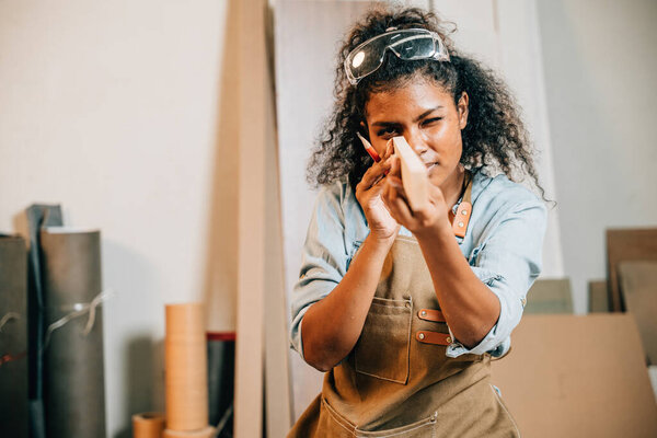 Carpenter woman holding and inspecting a piece of wood in a workshop, surrounded by tools and materials. Focused on woodworking and craftsmanship. National Carpenters Day celebration