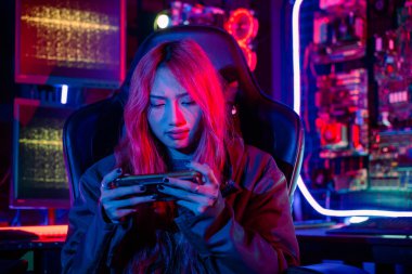 Asian woman live stream she play video game via smartphone at home neon lights living room, Gamer playing online game application on mobile phone wear gaming headphones, E-Sport concept