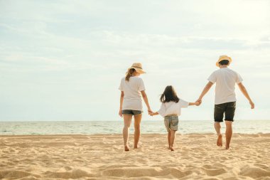 Mutlu Asyalı ebeveynler ve kızları sahilde eğleniyorlar. Anne ve babalarıyla birlikte kumsalda yürüyen bir çocuğun elini tutan küçük kızlar. Olumlu aile aktivitesi