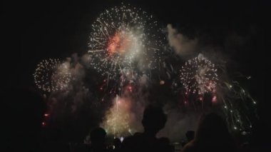 Pattaya 'da neşeli bir gece, havai fişeklerin gökyüzünü kırmızı, mavi ve sarı ışıklarla aydınlattığı, neşe ve kutlamaları simgeleyen.