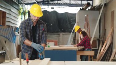 Sarı kasketli ve güvenlik gözlüklü marangoz atölyede iki tahta parçasına klemp takmış. İşçi Bayramı temaları için mükemmel, marangozluk uzmanlığı ve zanaatkarlığı vurgulanıyor