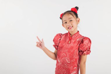 Neşe saçıyor, kırmızı Cheongsam elbiseli Asyalı bir kız tek parmağıyla emin bir şekilde işaret ediyor. Saçları kırmızı aksanlı, temiz beyaz arka plandaki neşeli havayı arttırıyor. Çin Yeni Yılı