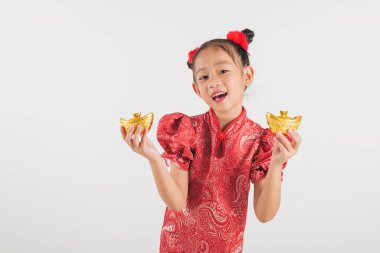 Kırmızı Cheongsam elbiseli, altın külçeli Asyalı bir çocuk. Beyaz bir arkaplanda, Çin Yeni Yıl geleneklerini kutluyor ve parlak gülümsemesiyle neşe ve refah yayıyor..