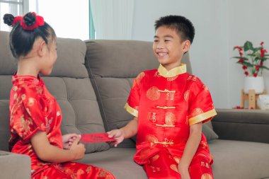 Kırmızı Cheongsam giyimli Asyalı kardeşler oturma odalarında uğurlu para için neşeyle kırmızı zarfları paylaşırlar. Sahne gelenek, mutluluk ve Çin Yeni Yılı ruhunu yansıtıyor..