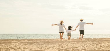 Mutlu Asyalı ebeveynler ve kızları sahilde eğleniyorlar. Kumda koşan ve rol yapan anne ve babalarıyla küçük kızlar. Olumlu aile aktivitesi