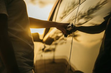 Gün batımında bir arabanın kapısını açan genç kadın elini kapat. Sürücü koltuğuna geçmek için el ele tutuşun. Seyahat konsepti