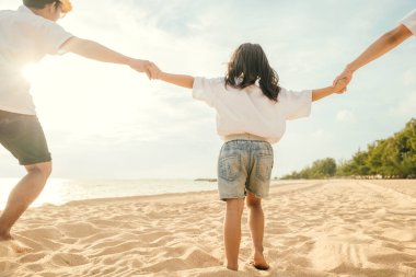 Mutlu Asyalı ebeveynler ve kızları sahilde eğleniyorlar. Kumda koşan ve rol yapan anne ve babalarıyla küçük kızlar. Olumlu aile aktivitesi