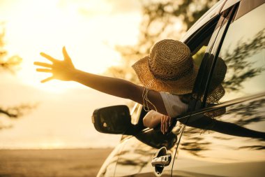 Şık şapkalı bir kadın gün batımında el sallayarak arabanın ön koltuğunda oturur ve rüzgarı hisseder. İyi hafta sonları. Plajda iyi tatiller. Yolculuk ve özgürlük kavramı
