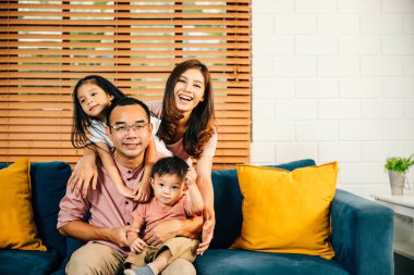 Neşeli bir Asyalı aile babası, anne ve kızı, modern evlerindeki rahat bir kanepede kendi yalnızlıklarını kucaklayan mutluluğu buluyorlar..