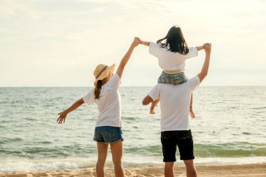 Tatilde mutlu bir aile. Baba, anne ve çocuklar yaz plajında omuz omuza geziyorlar, aileler çocukları sahilde boyuna taşıyorlar, aileler yaz tatilinin tadını çıkarıyorlar.