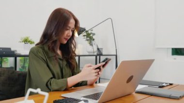 Mutlu güzel bir kadın masa başında oturmuş akıllı telefondan alışveriş yapıyor Asyalı genç iş kadını bilgisayarla çalışıyor ve ev telefonunda cep telefonuyla sohbet ediyor.
