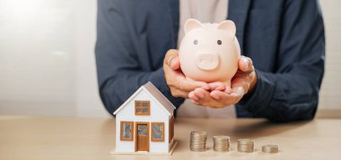 El ele tutuşan domuz kumbarası, model ev ve para tablosu, tasarruf, emlak yatırımı, ipotek stratejileri, etkin bankacılık ve vergi ile rüya ev sergilenen finansal planlama.
