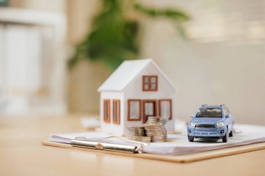 Belgelerin yanında ev ve araba modelleri gayrimenkul ve mali planlamayı ön plana çıkarıyor. Bankacılık, tasarruf ve gelecekteki varlıkların güvence altına alınması için yapılan yatırımların net bir temsili.