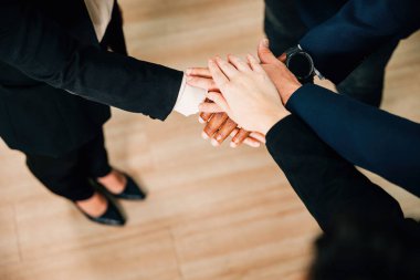 Yukarıda, modern bir ofiste takım çalışmasının, birliğin ve birlikteliğin gücünü vurgulayan el ele tutuşan iş adamları görülüyor. Toplantılar, beyin fırtınası ve başarı teşvik eder..