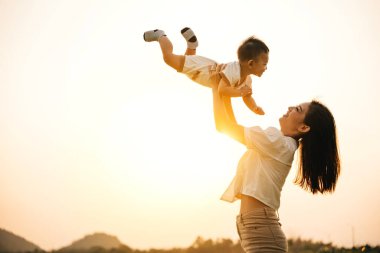 Kaygısız bir tatil gününde, bir anne ve çocukları doğada neşeli bir anın tadını çıkarırlar. Yüzlerinde gülümsemeyle ellerini havaya kaldırırlar ve bulutların arasında özgürce uçmanın tadını çıkarırlar.