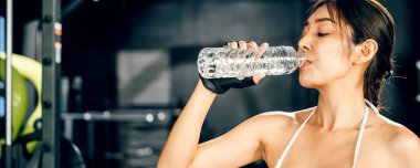 Kardiyo çalışmasından sonra şişeden su içen Asyalı kadın sporcu, spor salonunda antrenman yaptıktan sonra içki içen kadın, sağlıklı yaşam tarzı kavramı.